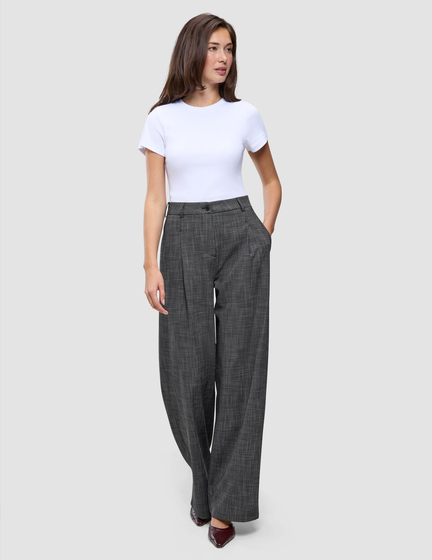 Eine Frau trägt ein weißes T-Shirt und die Hose Women Nara Pants Wide Black Check mit hoher Taille und dezentem Karomuster.